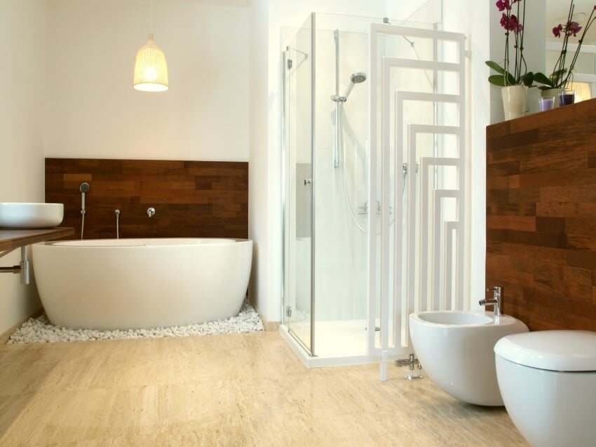 Белая ванная комната с отдельно стоящей ванной, деревянной акцентной стеной и травертиновым полом