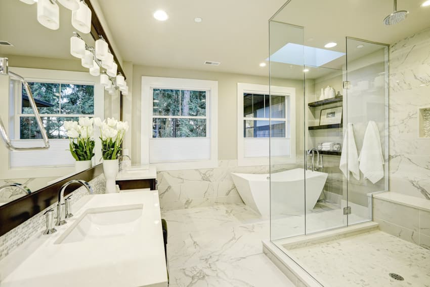 Ванная комната со стенами и полами из каррарского мрамора, стеклянной душевой кабиной, раковиной, столешницей, окнами и зеркалом.