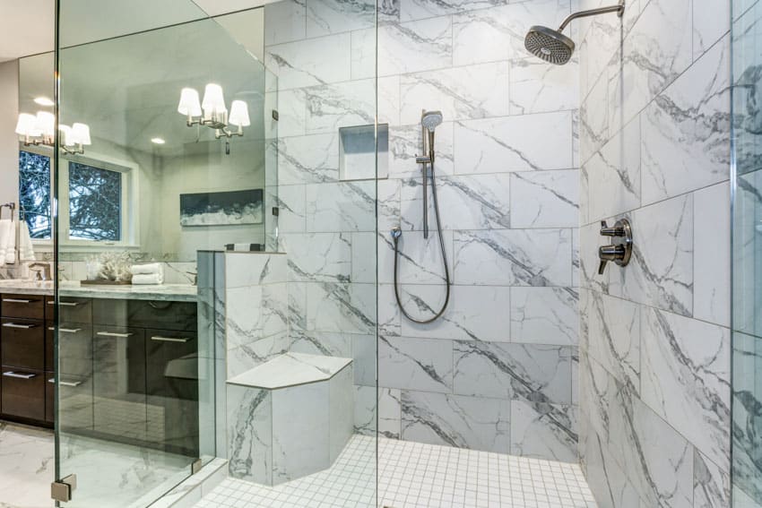 Ванная комната со стеной, выложенной плиткой из каррарского мрамора, душем, туалетным столиком, зеркалом, столешницей и выдвижными ящиками.