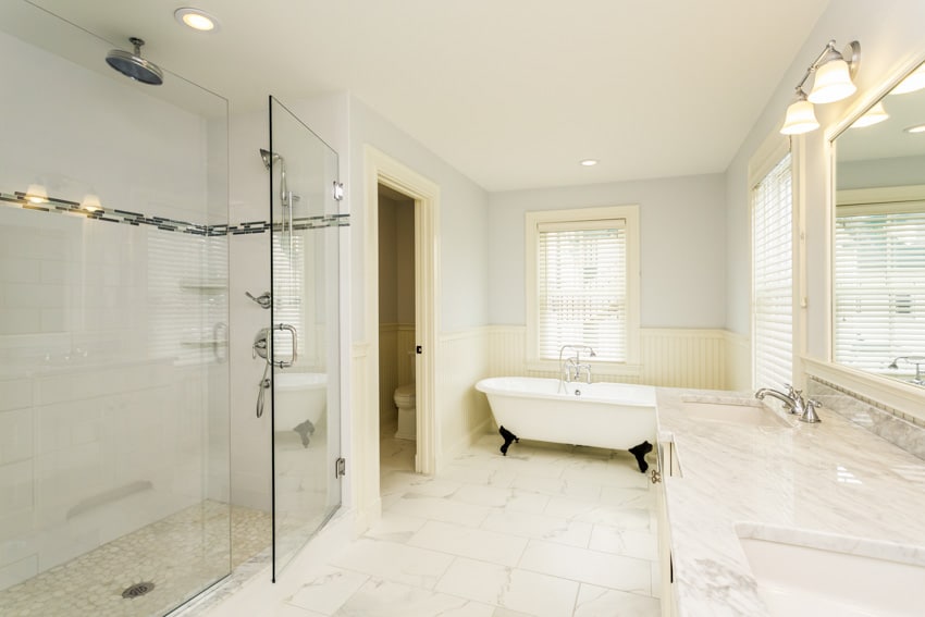 Ванная комната с полом из каррарского мрамора, стеклянной дверью, душем, столешницей, зеркалом и окном.