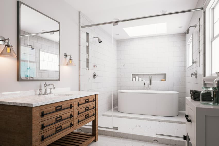 Ванная комната с плиткой из каррарского мрамора, ванной, столешницей, туалетным столиком, зеркалом, ящиками и окнами.