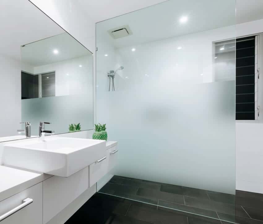 Чистая ванная комната с белыми стенами, черной напольной плиткой и частично матовыми стеклянными дверями душа