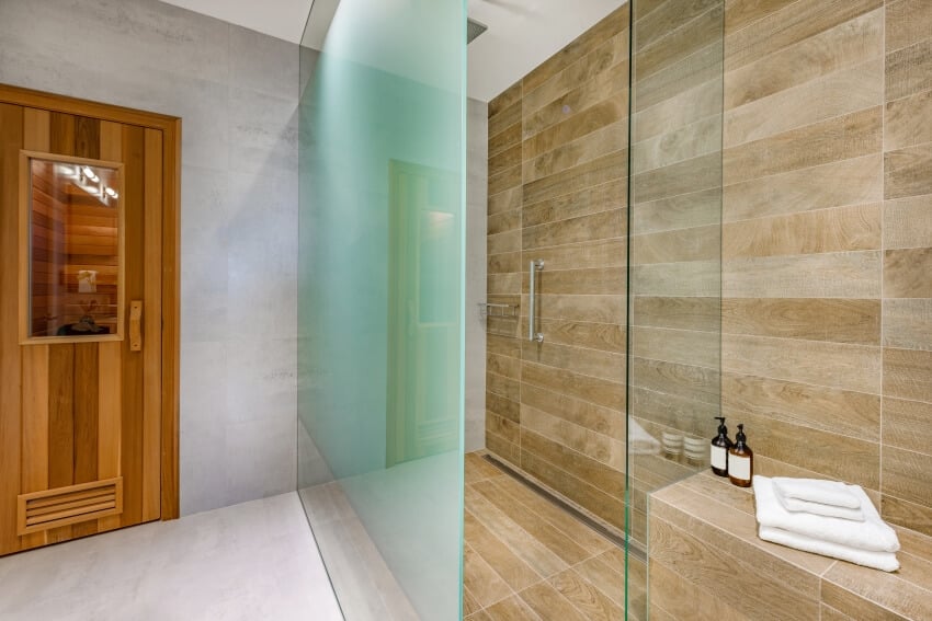 Красивый современный дизайн ванной комнаты с матовыми стеклянными душевыми дверями и деревянным полом и настенной плиткой.