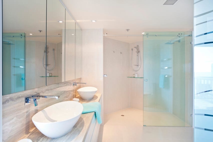 Чистый кремовый интерьер ванной комнаты с двумя умывальниками и душем с раздвижными дверьми из матового стекла