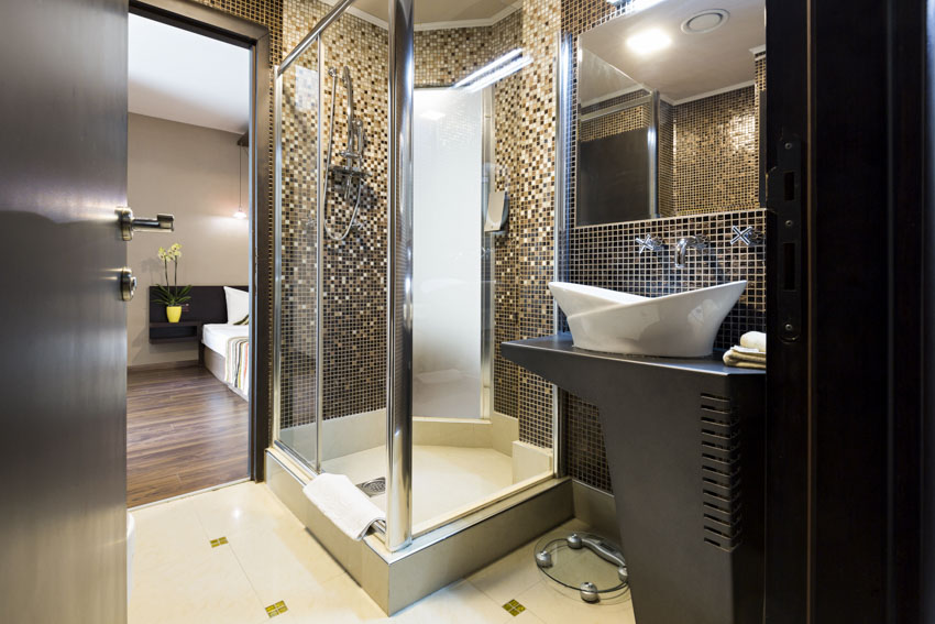 Ванная комната с душевой кабиной, душевой стеной из мозаичной плитки, зеркалом и раковиной.