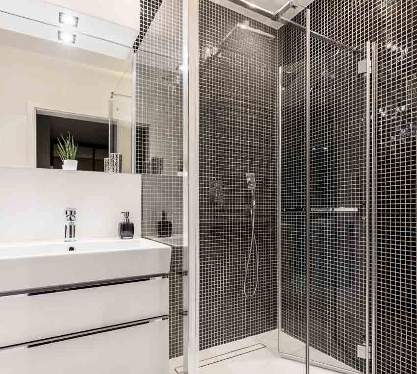 Ванная комната с душем из черной стеклянной плитки, стеклянной дверью, раковиной, краном и зеркалом.