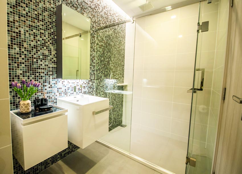 Ванная комната с душевой кабиной из зеленой стеклянной мозаики, туалетным столиком, стеклянной дверью, раковиной и зеркалом.