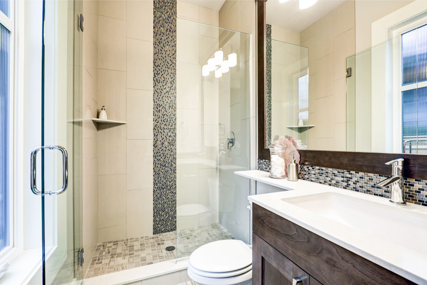 Ванная комната с водопадной мозаикой, душевой стеной, стеклянной дверью, косметическим зеркалом, столешницей и туалетом.