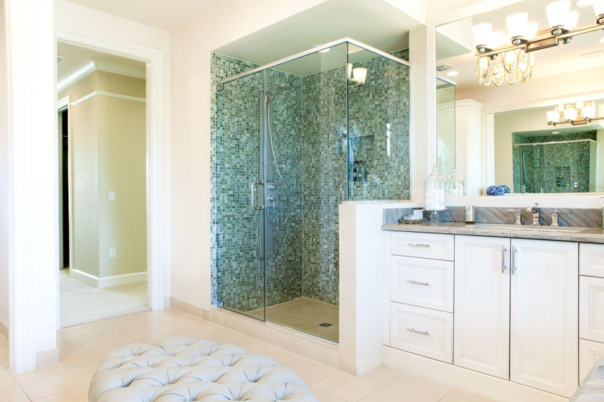 Ванная комната со стеклянной мозаичной душевой плиткой, шкафами, столешницей, зеркалом и ковриком на полу