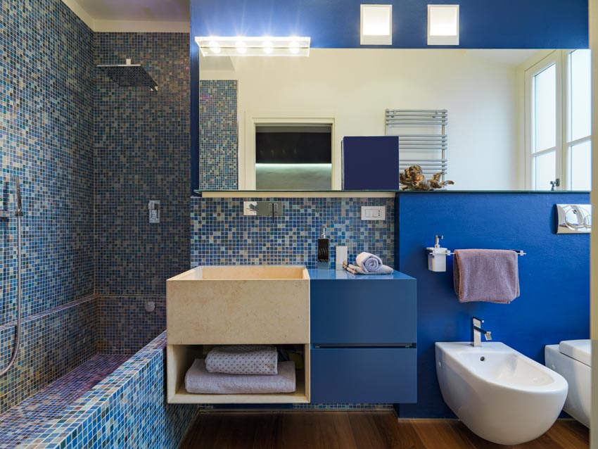 Ванная комната с синей мозаичной плиткой, душевой стеной, раковиной, косметическим зеркалом и туалетом
