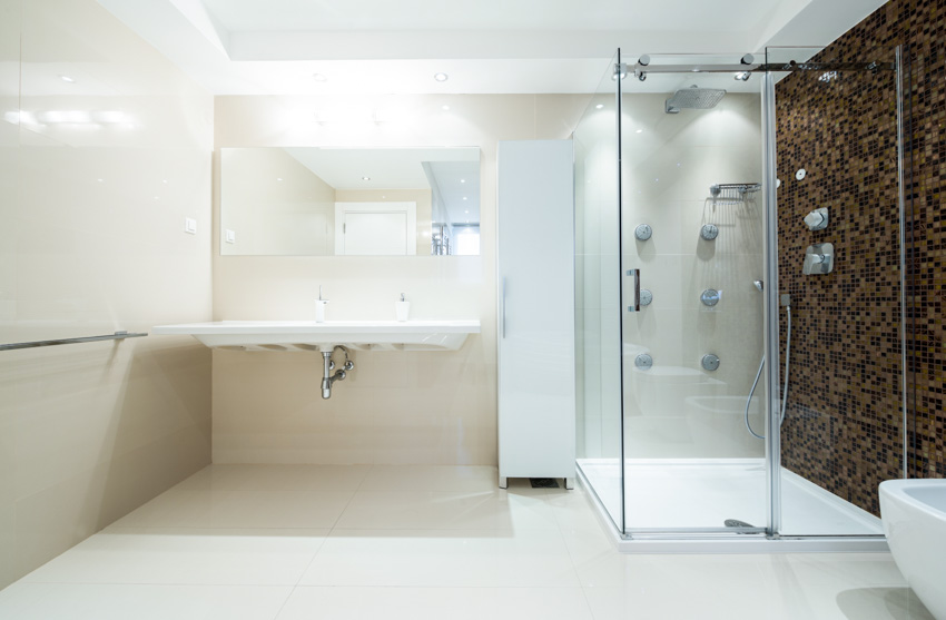 Ванная комната со стеклянным ограждением, душевой стеной, выложенной мозаичной плиткой, плавающей раковиной и зеркалом.