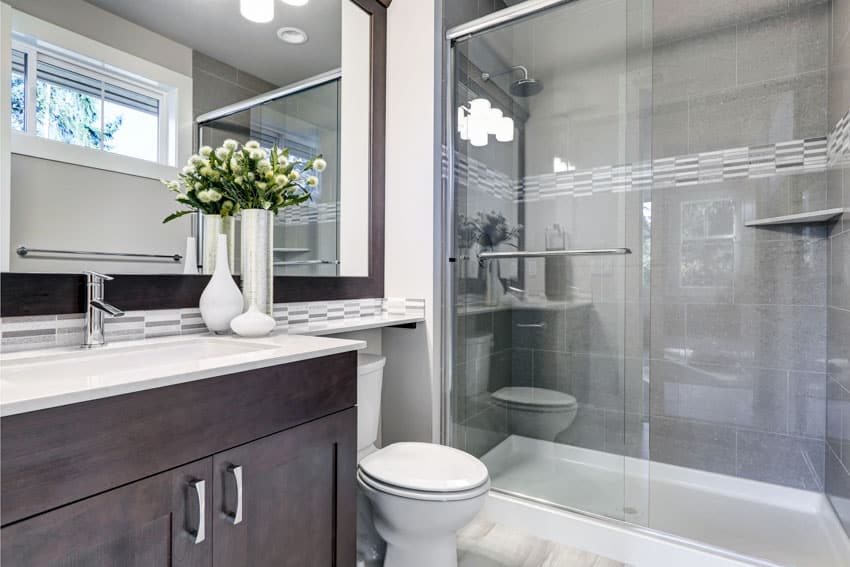 Ванная комната со стеклянными раздвижными душевыми дверями, душевой стеной из плитки, туалетным столиком, столешницей, шкафчиками и зеркалом.