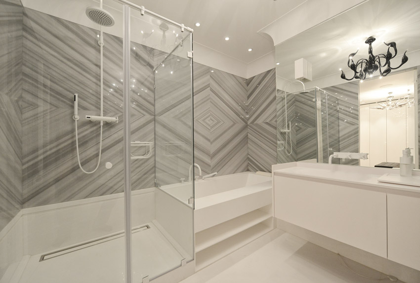 Ванная комната с красивой крупноформатной плиткой, душевой стенкой, ванной, стеклянным ограждением, столешницей, зеркалом и насадкой для душа.