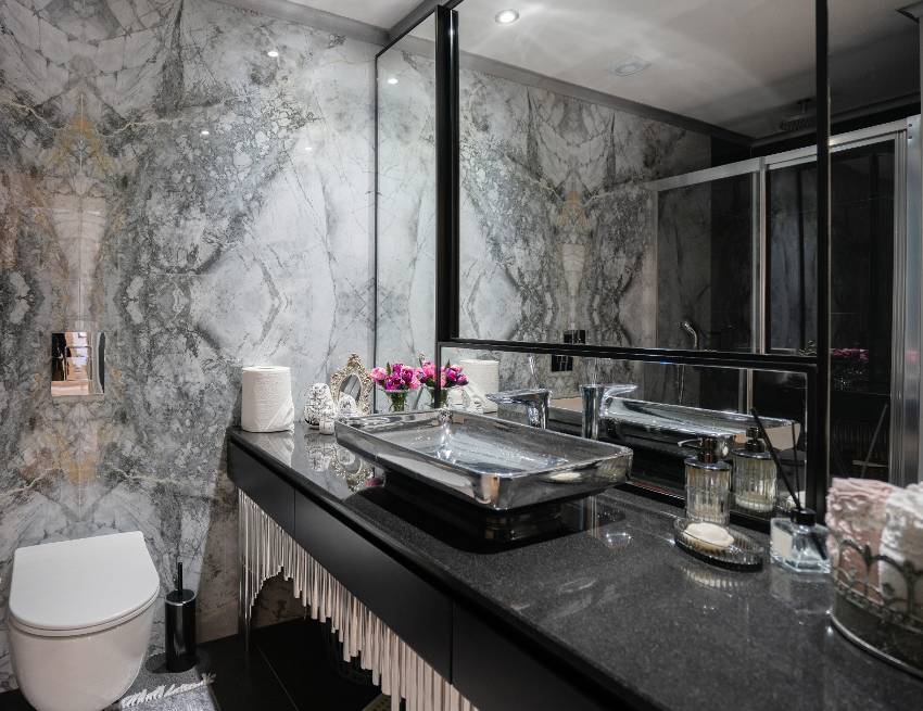 Красивый дизайн ванной комнаты из темного мрамора с современной сантехникой и столешницей из гранита черного цвета.