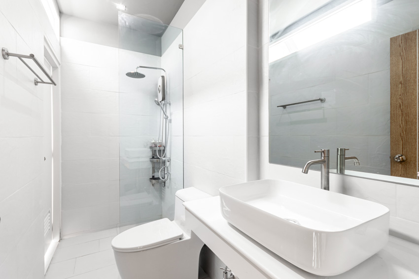 Ванная комната с керамической душевой стенкой, стеклянной перегородкой, столешницей, раковиной, зеркалом, унитазом и держателем для полотенец.