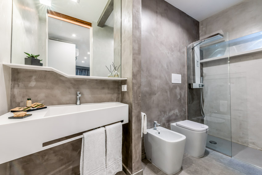 Ванная комната с эпоксидной стенкой для душа, туалетом, биде, стеклянной перегородкой, плавающей раковиной и зеркалом.