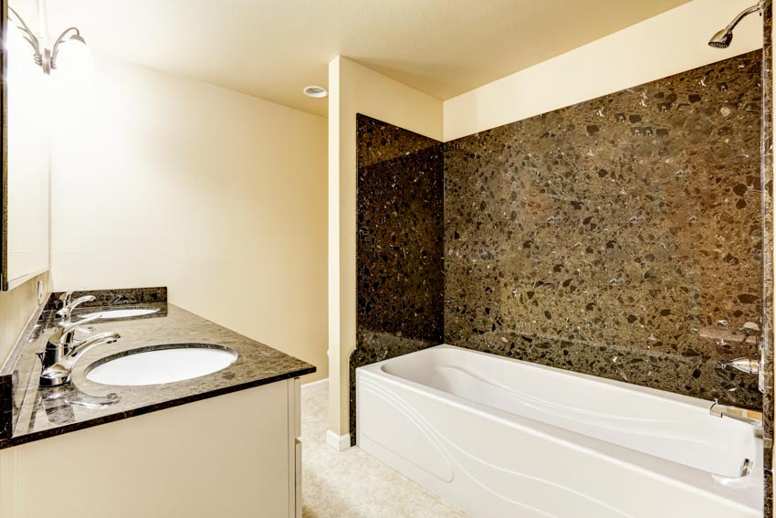 Ванная комната с гранитной душевой стеной, ванной, столешницей, раковиной и насадкой для душа.