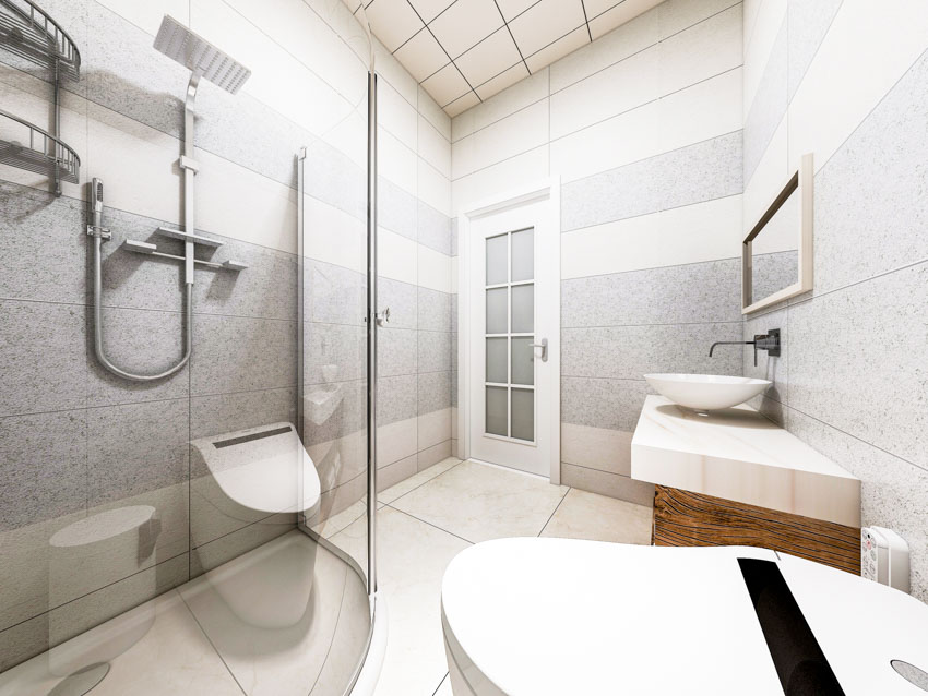 Ванная комната с душем, стеклянной перегородкой, туалетом, раковиной, зеркалом, потолочной плиткой и гранитной душевой стеной.