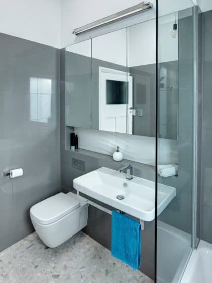 Маленькая ванная комната с серыми керамическими плитками и белыми туалетами