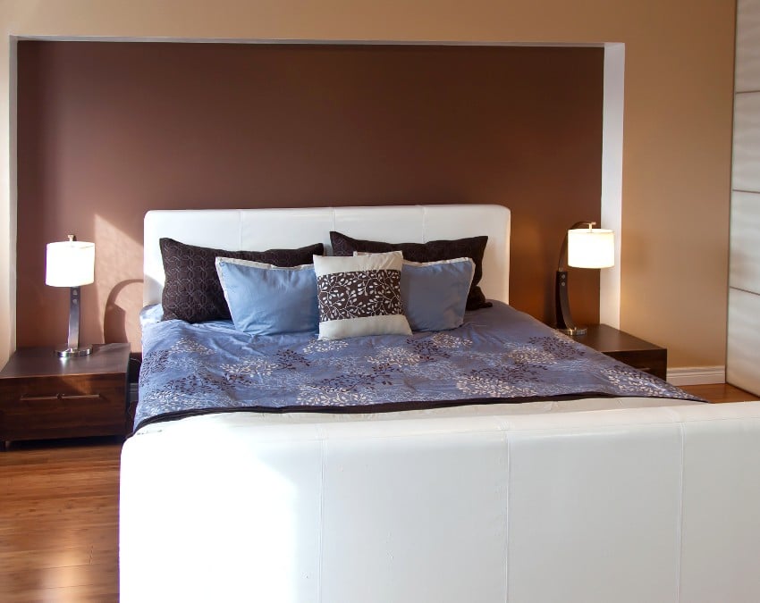 Дизайн интерьера спальни с коричневыми стенами эспрессо, деревянными полами и белой кроватью
