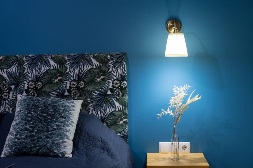 Спальня с настенным бра, тумбочкой, подушкой, изголовьем и окрашенной в синий цвет стеной