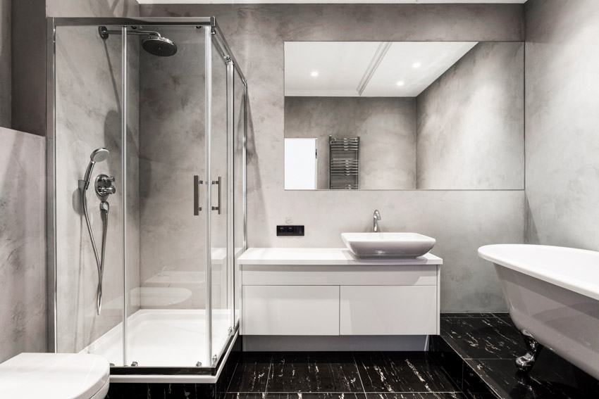 Ванная комната с чугунным поддоном для душа, черным плиточным полом, туалетным столиком, столешницей, зеркалом, раковиной, стеклянной душевой кабиной и ванной.