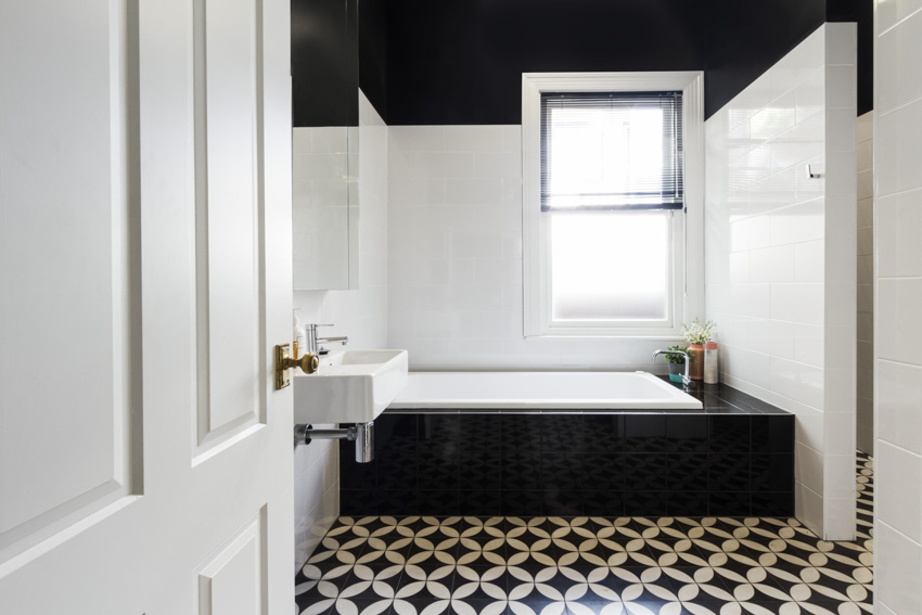 Ванная комната с черно-белой напольной плиткой, ванной, окном, раковиной и зеркалом