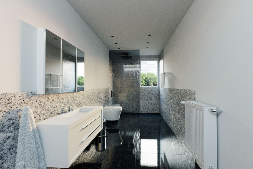 Гранитная стена ванной комнаты, пол из глянцевой черной плитки, туалетный столик, зеркало и туалет.