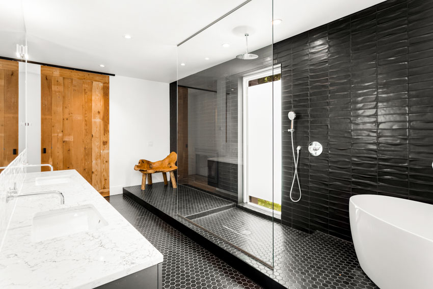 Ванная комната с черной шестиугольной напольной плиткой, душем, ванной, стеклянной перегородкой, окном, раковиной, столешницей и деревянной дверью