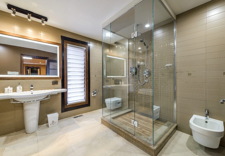 Удивительный интерьер ванной комнаты с кафельным полом, раковиной на пьедестале, туалетом, стенами внахлест и душем, закрытым стеклом и потолочной плиткой.