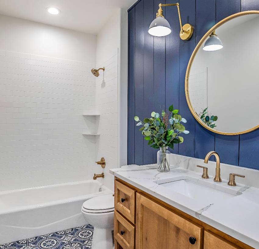 Потрясающая современная ванная комната с ванной, круглым зеркалом на акцентной стене и латунными светильниками.