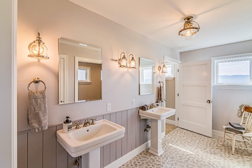 Красивая ванная комната с серой акцентной стеной, двойными раковинами на пьедестале и несколькими бра