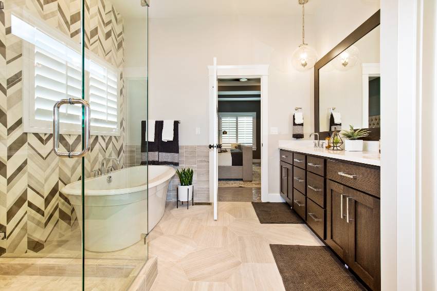 Великолепная ванная комната с ванной, деревянными шкафами, кафельным полом и акцентной стеной из виниловых обоев.