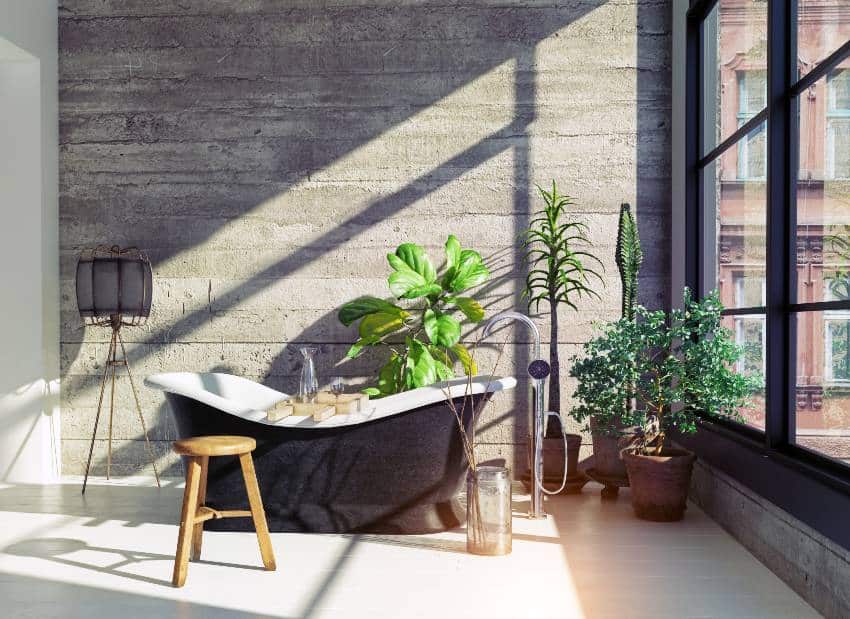 Современная ванная комната в индустриальном стиле с массивной бетонной стеной, отдельно стоящей ванной, естественным освещением и большими окнами.