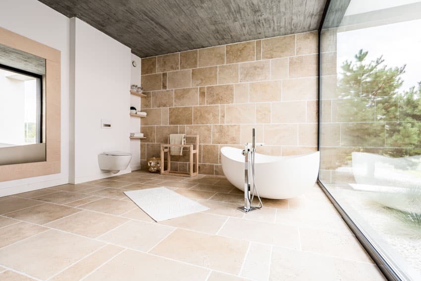 Ванная комната с текстурированной керамической плиткой от пола до потолка, ванной, туалетом, плавающими полками и окном.