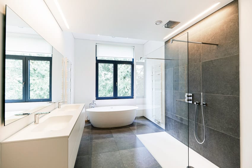 Ванная комната с душевой кабиной от пола до потолка, стеклянным ограждением, ванной, столешницей, зеркалом и окнами.