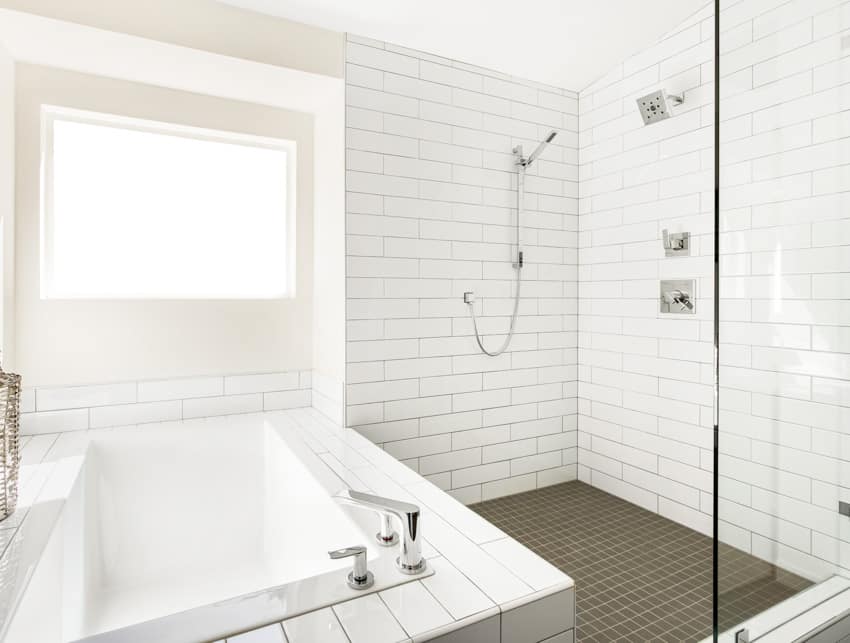 Ванная комната с плиткой от пола до потолка, окном, двойным душем и ванной.