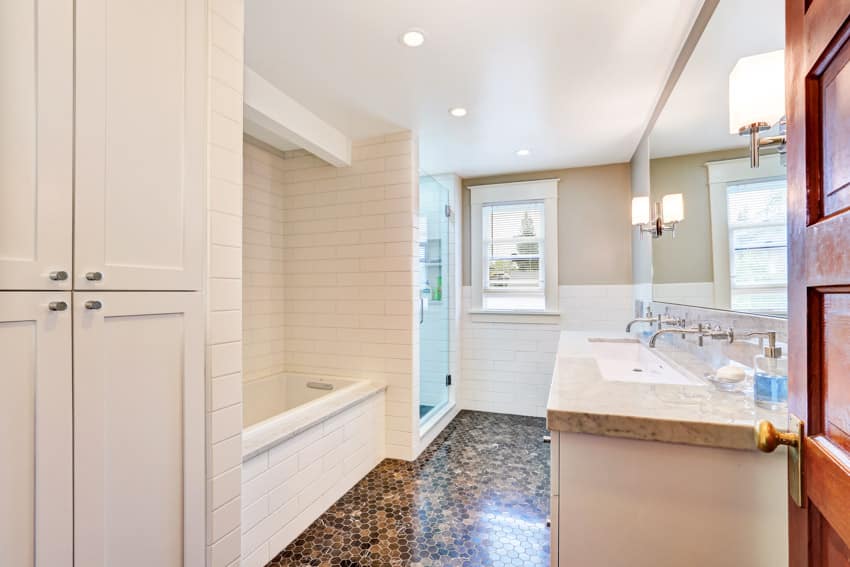 Ванная комната с плиткой от пола до потолка, ванной, окном, туалетным столиком, потолочными светильниками, столешницей и зеркалом.