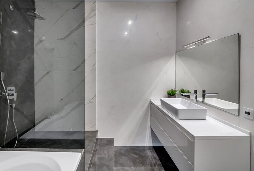 Интерьер современной ванной комнаты с мраморными стенами, столешницей из ламината и серыми кафельными полами