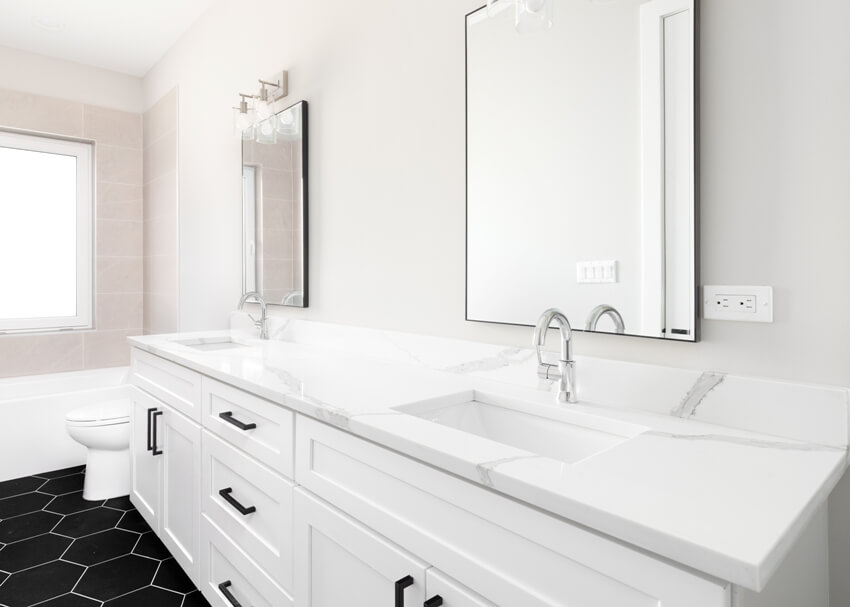 Великолепная ванная комната с белыми тумбочками и столешницей из ламината и мрамора, полом из черной шестиугольной плитки и душем из коричневой плитки.