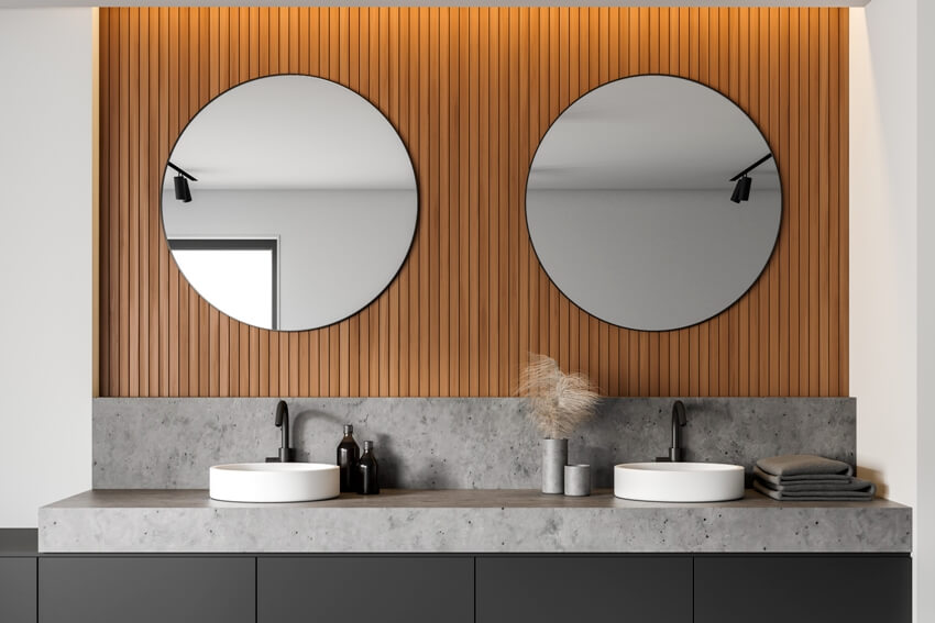 Крупный план двойной раковины в ванной на столешнице из бетонного ламината в стильной комнате с белыми и деревянными стенами и двумя круглыми зеркалами