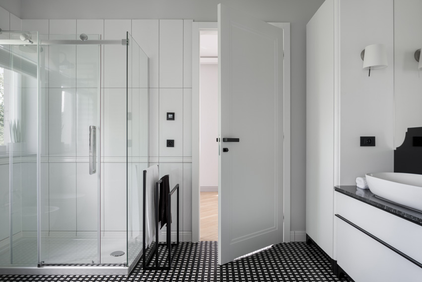Ванная комната с вертикальной душевой кабиной большого формата, стеклянным ограждением, черным полом, дверью, раковиной и белыми стенами
