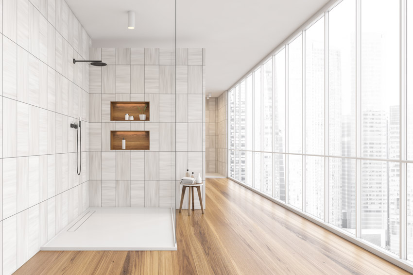 Красивая ванная комната с плиткой большого формата, душем, деревянным полом и окнами
