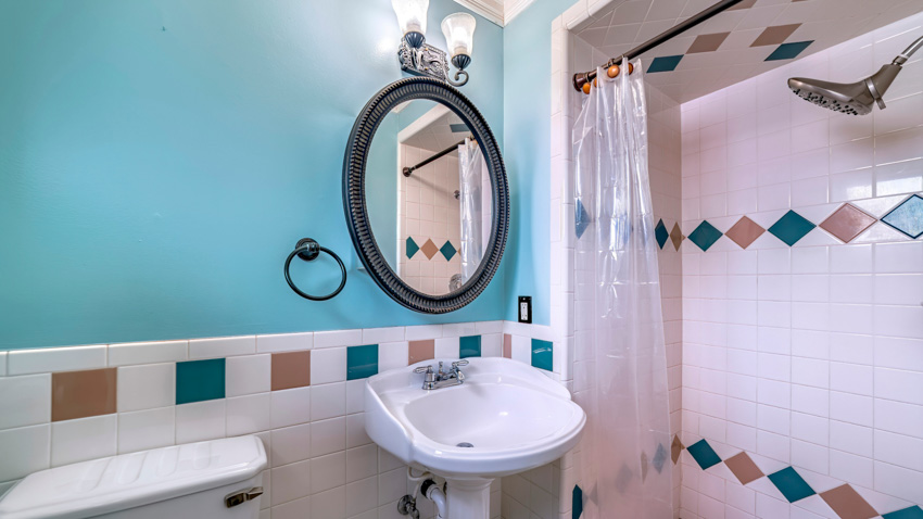 Ванная комната с пластиковой занавеской для душа, плиточной стеной, зеркалом, раковиной и настенными светильниками.