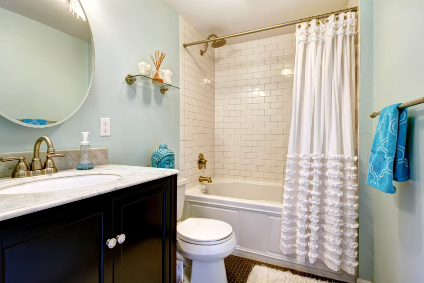 Ванная комната с занавеской для душа с рюшами, душевой стеной из плитки, туалетом, зеркалом и столешницей.