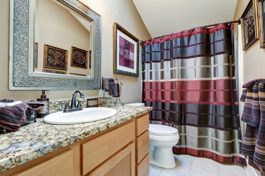 Ванная комната с утяжеленной занавеской для душа, гранитной столешницей, раковиной, зеркалом и унитазом.