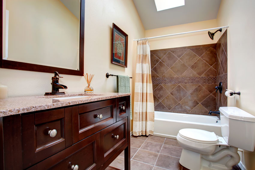 Ванная комната с кафельной душевой стеной, занавеской для душа, ящиками, столешницей, зеркалом, туалетом и плиточным полом.