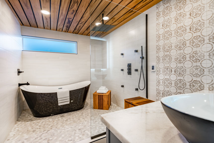 Ванная комната с душевой кабиной, ванной, акцентной стеной с плиткой, деревянным потолком и раковиной.
