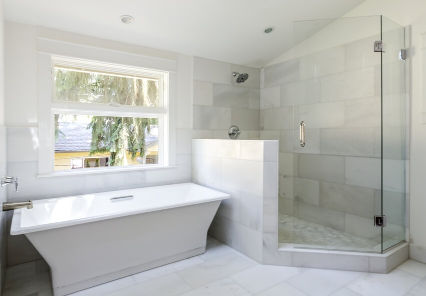 Современная ванная комната, отделанная мраморной плиткой, с открытой душевой кабиной с пони-стеной и ванной.