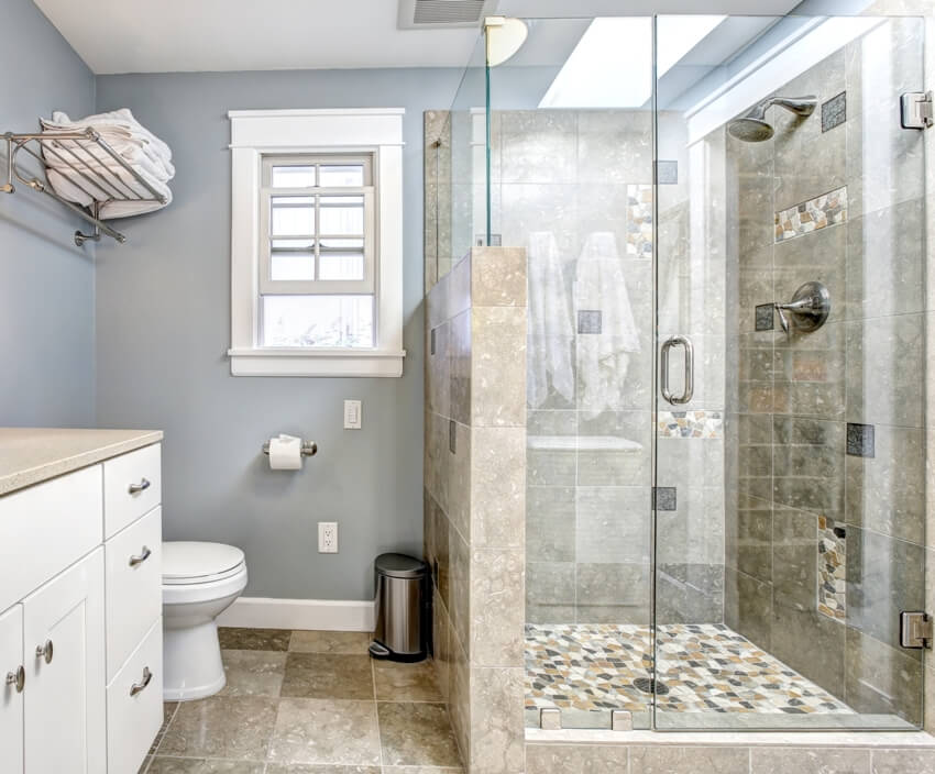 Светло-голубой современный интерьер ванной комнаты со стеклянной дверью, настенным душем пони и белым шкафом с зеркалом